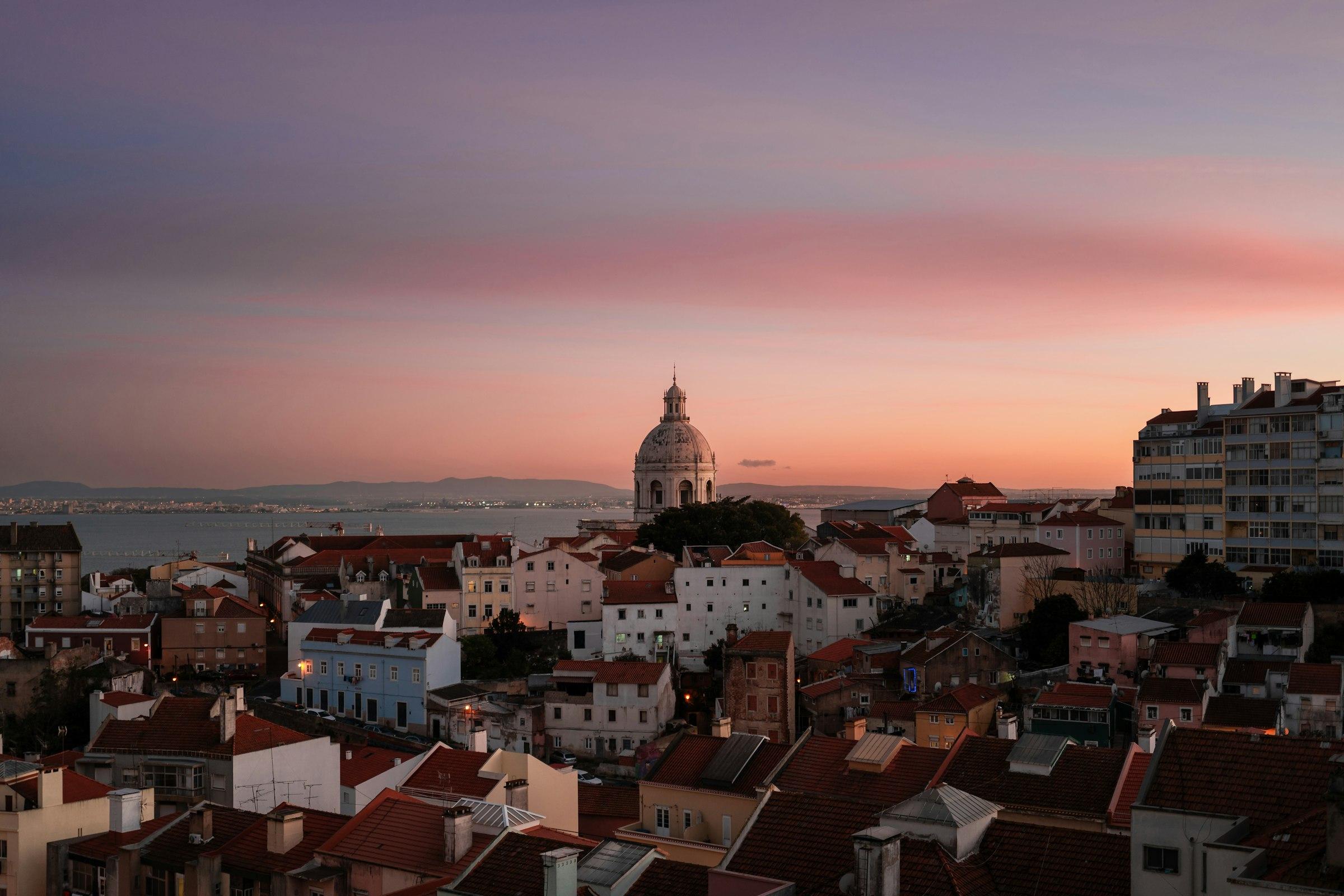 Rooftops of Lisbon's Alfama district glowing at sunset, seen from a window above the city